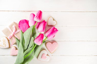 Sevgililer Günü konsepti, Bahar Kadınları Günü Tatili, Anneler Günü arkaplanı, Kırmızı lale çiçeği buketi, el işi kağıt hediye kutusu, kalp şeklinde geleneksel şeker kurabiyeleri, beyaz ahşap arka plan kopyalama alanı.
