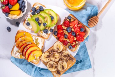 Meyveli sandviç. Fıstık ezmeli, krem peynirli çeşitli tostlar, yaz meyveleri ve meyveli çikolata - çilek, muz, şeftali, elma, yabanmersini, lezzetli öğle yemeği