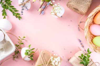 Eco friendly zero waste Easter flatlay. Spring flowers, leaves, eggs on pink pastel background, with craft paper gift box. Woman hands decorate eggs with organic natural decor, preparation for Easter