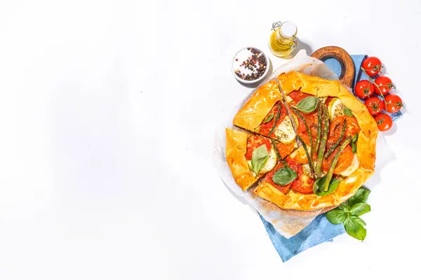 Fresh baked homemade vegetable vegan pie, Crunchy savoury galette tart  with olives, zucchini, tomatoes, asparagus, with ingredients for cooking, spices, olive oil