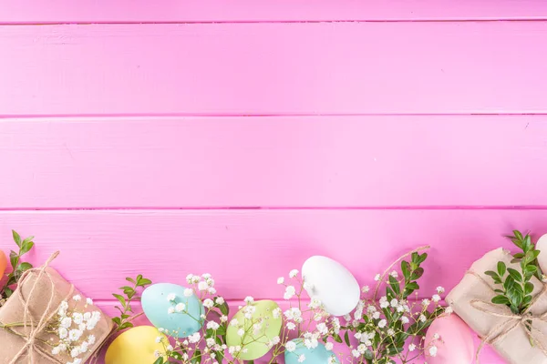 Pink Easter greeting card background with spring flowers, green leaf branches and colorful pastel Easter eggs, top view copy space