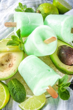 Ev yapımı avokado dondurması. Vejetaryen sütsüz dondurma. Avokado, kireç ve hindistan cevizi. Gri taş zemin üzerinde sağlıklı buzlu dondurma. Taze limon dilimleri, avokadolar ve buz.