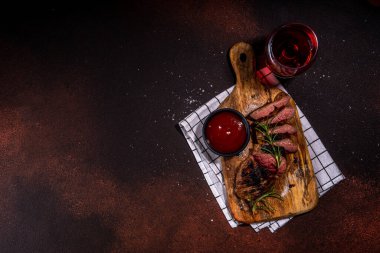 Grilled meat steak on dark table, Pork, veal, lamb, beef steak medium, medium well on cutting board, with spices, ketchup bbq sauce, wine glass. Dinner in steak restaurant menu, top view copy space