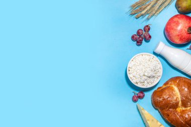 Yahudi bayramının sembolleri olan mutlu Shavuot tebrik kartı - nar, üzüm, elma, tatlı challah ekmeği, buğday filizi, süt, peynir, süzme peynir, açık mavi zemin
