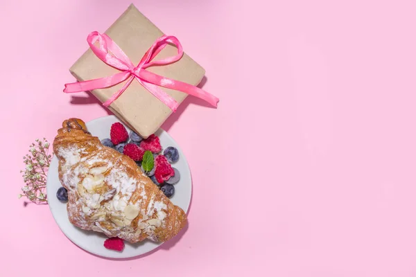 Croissant with coffee and Valentines gift and coffee latte mug on pink background copy space. Valentine day, Mother day sweet tasty breakfast idea. Good morning and nice spring, summer day concept