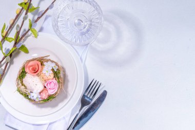 Easter table setting. Festive spring holiday cutlery set, with plate, wine glass, knife, fork, with Easter decor egg nest, willow flower branches, white sunny table background copy space top view