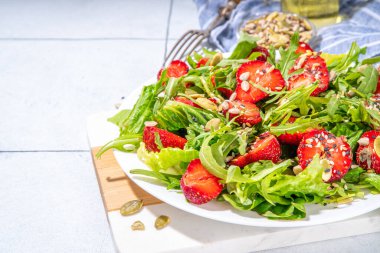 Yaz sağlıklı yemekleri, çilekli roka salatası. Taze diyet çilek salatası roka, ıspanak, marul, çeşitli fındık ve tohumlar, beyaz fayans arka planında fotokopi alanı