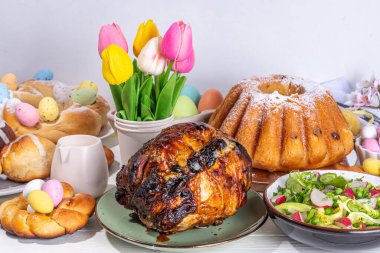 Festivalde Paskalya yemeği veya brunch masası sunuldu, Paskalya yumurtası, lale çiçeği buketi, geleneksel Paskalya yemekleri - pasta, çapraz çörekler, çelenk ekmeği, jöleli jambon ve bahar salatası, beyaz masa arkaplanı