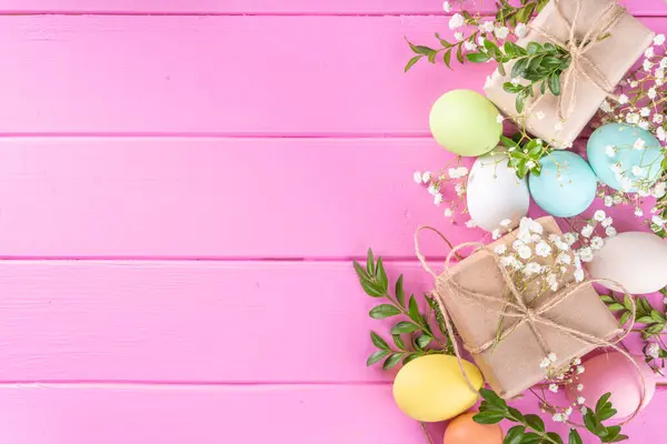 Pink Easter greeting card background with spring flowers, green leaf branches and colorful pastel Easter eggs, top view copy space