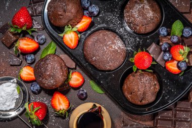 Çilekli çikolatalı kek. Kakao soslu ev yapımı çikolatalı kek tepsisi, şeker tozu ve taze çilek, yabanmersini, koyu kahverengi arka plan fotokopi alanı.