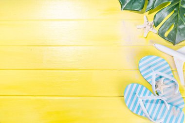 Bright sunny lighted summer vacation background, vacation and travel, beach accessories, swim suit, hat, flip flops, photo camera, sea star and shells on high-colored yellow wooden background top view