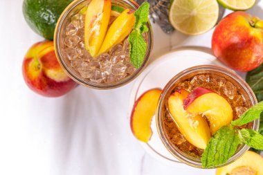 Buzlu şeftali çayı, ya da limonlu şeftali limonatası, nane, ezilmiş buz ve altın bej arka planda bar aletleri. 