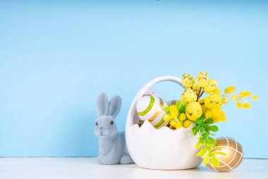 Tatlı Paskalya bayramı tebrik kartı geçmişi. Renkli Paskalya yumurtaları sepetin içinde tavşan dekoru, bahar çiçekleri beyaz tahta masa arka planında, kopyalama alanı