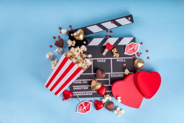Romantic date on Valentine's Day February 14. Love movie marathon, date at cinema theater. Clapperboard, popcorn buckets, heart decor and chocolates on red background flat lay copy space