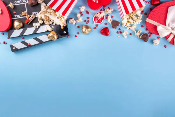 Romantic date on Valentine\'s Day February 14. Love movie marathon, date at cinema theater. Clapperboard, popcorn buckets, heart decor and chocolates on red background flat lay copy space