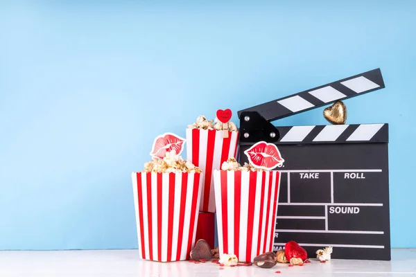 Romantic date on Valentine's Day February 14. Love movie marathon, date at cinema theater. Clapperboard, popcorn buckets, heart decor and chocolates on red background flat lay copy space