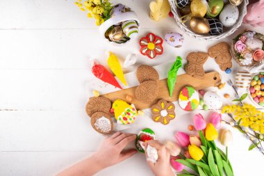 Paskalya için aile hazırlığı. Tatil pişirme arka planı, kadın ve çocuk elleri ev yapımı kurabiyeleri şekerle süsler, paskalya yumurtaları, tavşanlar, çiçekler, üst görünüm kopya alanı şeklinde.