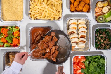 Yemek pişirme konsepti. Çeşitli çeşit mezeler: tahıl gevreği, makarna, makarna, pişmiş ve taze sebzeler, et, tavuk, nugget, kahvaltı krepleri ve yiyecek kabında meyve. 