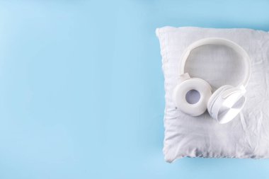 Rahat kulaklıklar ve açık mavi arka planda beyaz yastıkla uyku konsepti için sonik renkler ve gürültü.