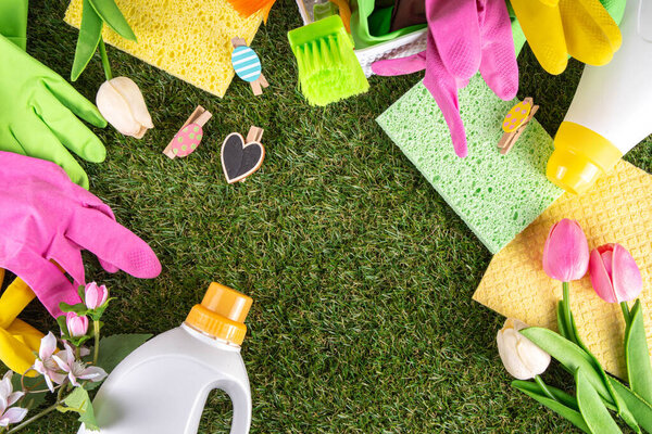 Весенняя уборка фона. Комплект чистящих средств, бутылок, аксессуаров и вещей с весенними цветами в корзине на белом деревянном зеленом саду