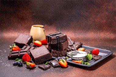 Böğürtlenli siyah çikolatalı kek. Üzerine çikolata sosu serpiştirilmiş ev yapımı kek kurabiyeleri ve koyu arkaplanda taze çilek, yabanmersini, fotokopi alanı.