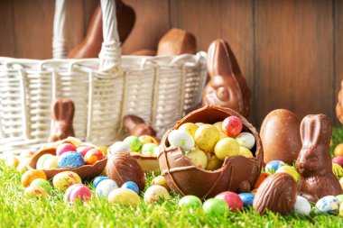 Easter egg hunting background. Various candy and chocolate Easter eggs, bunny and rabbits with basket for eggs on green grass park or garden background