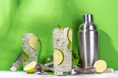 Klasik yaz soğuk mojito kokteyli, limonlu limonata, nane, ezilmiş buz ve beyaz arka planda bar aletleri.