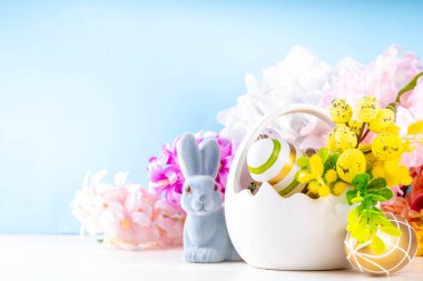 Tatlı Paskalya bayramı tebrik kartı geçmişi. Renkli Paskalya yumurtaları sepetin içinde tavşan dekoru, bahar çiçekleri beyaz tahta masa arka planında, kopyalama alanı