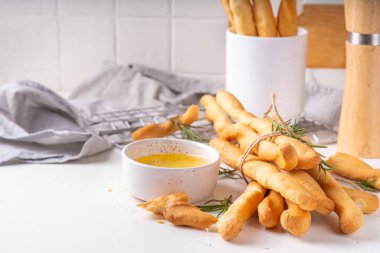 İtalyan Akdeniz Grissini ekmek çubukları, beyaz mutfak arka planında aromatik yağ ve biberiye filizleri ile