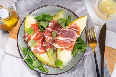 Prosciutto hamon ve yeşil yapraklı taze kavun salatası karışımı, sonbahar meyve sebze salatası, tabakta porsiyon, beyaz mermer arka plan fotokopi alanı.