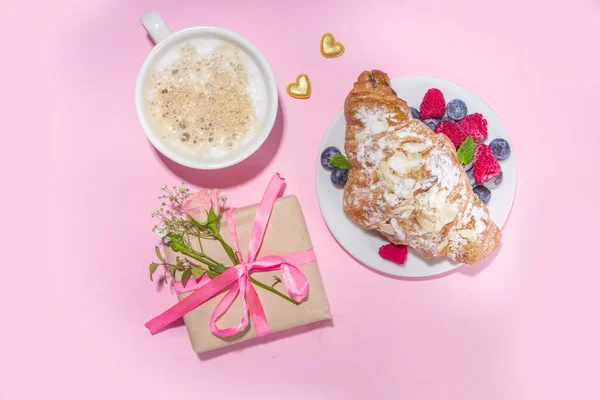 Croissant with coffee and Valentines gift and coffee latte mug on pink background copy space. Valentine day, Mother day sweet tasty breakfast idea. Good morning and nice spring, summer day concept