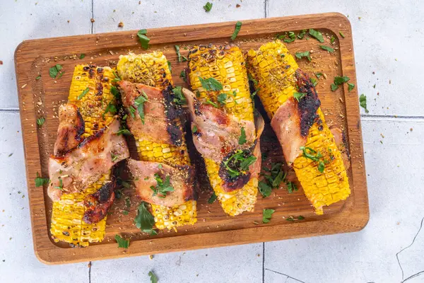 Bacon wrapped grilled corn on the cob, southern american, mexican bbq food recipe, with sauces on white tile background