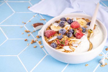 Lezzetli sağlıklı dengeli kahvaltı veya meyveli yoğurt tanecikleri - muz, çilek, yabanmersini, badem, hindistan cevizi dilimleri kopyalama alanı