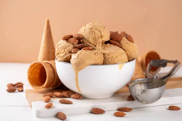 Almond nuts tasty caramel ice cream. Big bowl with gelato scoops and a lot of almonds on table background