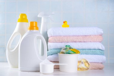 Çamaşır, çamaşır ve temizlik konsepti. Bir yığın temiz havlu, çeşitli deterjanlar - jeller, kapsüller, toz, çamaşır sepeti ve sevimli sarı ördek, beyaz banyo arka plan fotokopisi