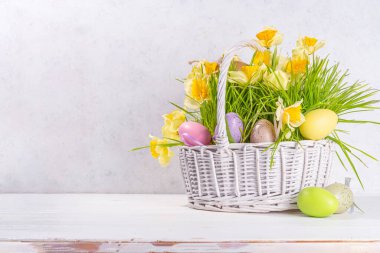 Easter greeting card background, banner format. Festive white basket with green grass, spring flowers bouquet, colorful Easter eggs, woman hands in picture take basket side view