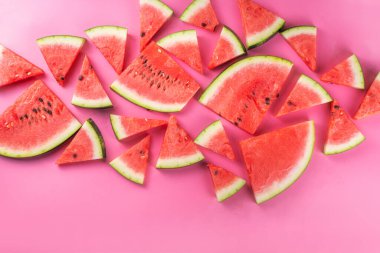 Renkli pembe arka planda dizilmiş karpuz dilimleri. Basit yaz hasadı ve tatil geçmişi, en üstteki düz görünüm afiş alanı