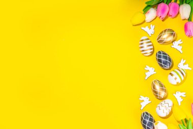 Parlak Paskalya tebrik kartı geçmişi. Renkli siyah, altın renkli, çizgili, beyaz tavşan desenli Paskalya yumurtaları, yüksek renkli sarı arka planda lale çiçeği, düz kopya alanı