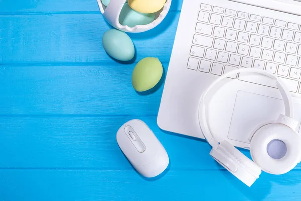 Easter office workplace, preparation for holiday, spring Easter sale, blogging. White laptop keyboard with easter eggs basket and flower branch decorations, on light blue wooden table top view