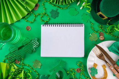 Saint Patrick masa takımı çatal bıçak, bıçak ve çatal, Patrick günü dekorasyonu, bozuk paralar, leprikon şapkası, gözlükler, şanslı at nalı, konfeti, yeşil arka planda boncuklar.