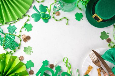 Saint Patrick masa takımı çatal bıçak, bıçak ve çatal, Patrick günü dekorasyonu, bozuk paralar, leprikon şapkası, gözlükler, şanslı at nalı, konfeti, yeşil arka planda boncuklar.