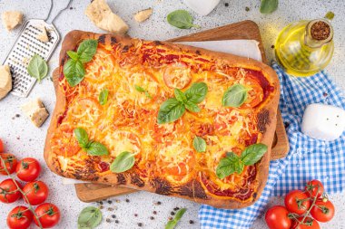 Domates ve fesleğenli ev yapımı margarita pizza, malzemeler ve arka planda beyaz mutfak masasında zeytinyağı.