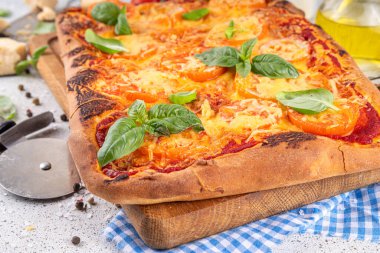 Domates ve fesleğenli ev yapımı margarita pizza, malzemeler ve arka planda beyaz mutfak masasında zeytinyağı.