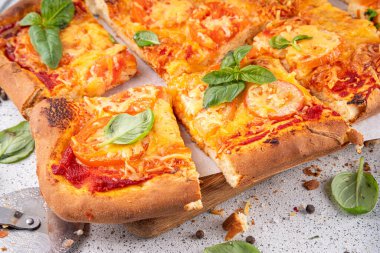 Domates ve fesleğenli ev yapımı margarita pizza, malzemeler ve arka planda beyaz mutfak masasında zeytinyağı.