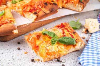 Domates ve fesleğenli ev yapımı margarita pizza, malzemeler ve arka planda beyaz mutfak masasında zeytinyağı.