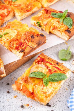 Domates ve fesleğenli ev yapımı margarita pizza, malzemeler ve arka planda beyaz mutfak masasında zeytinyağı.