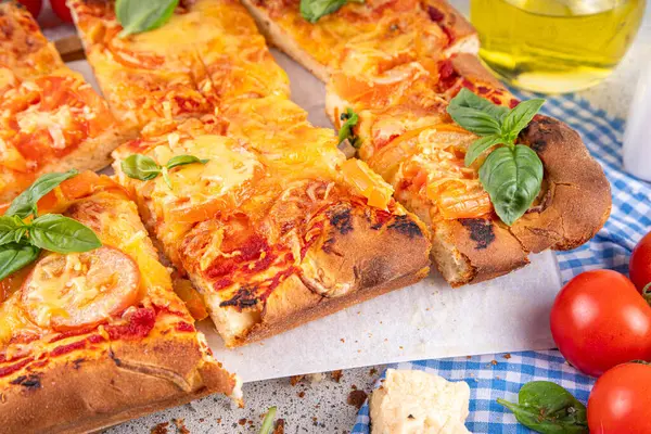 Rectangular homemade margarita pizza with tomatoes and basil, with ingredients and olive oil on white kitchen table background