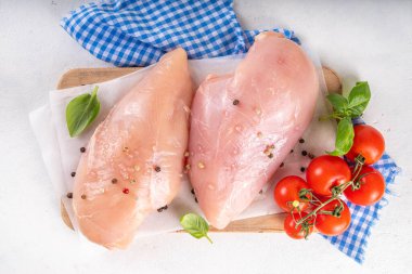 Mutfak masasında çiğ tavuk göğsü filetosu ve baharatlar. Beyaz yağsız et pişirme arka planı, beyaz masa kopyalama alanı
