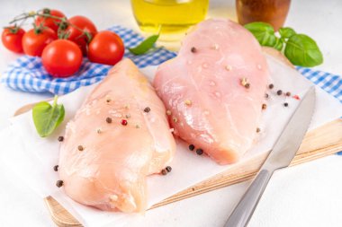 Mutfak masasında çiğ tavuk göğsü filetosu ve baharatlar. Beyaz yağsız et pişirme arka planı, beyaz masa kopyalama alanı