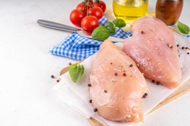 Mutfak masasında çiğ tavuk göğsü filetosu ve baharatlar. Beyaz yağsız et pişirme arka planı, beyaz masa kopyalama alanı